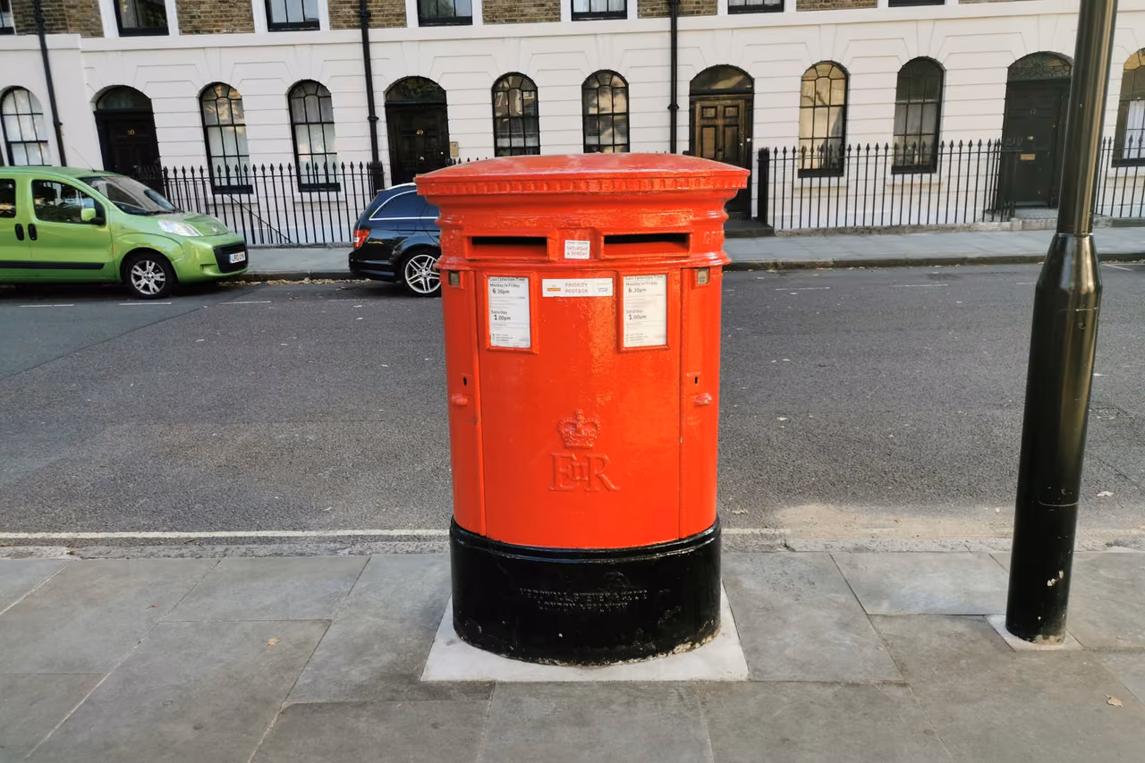 Red British pillar box on a pavement in front of a row of terraced houses
